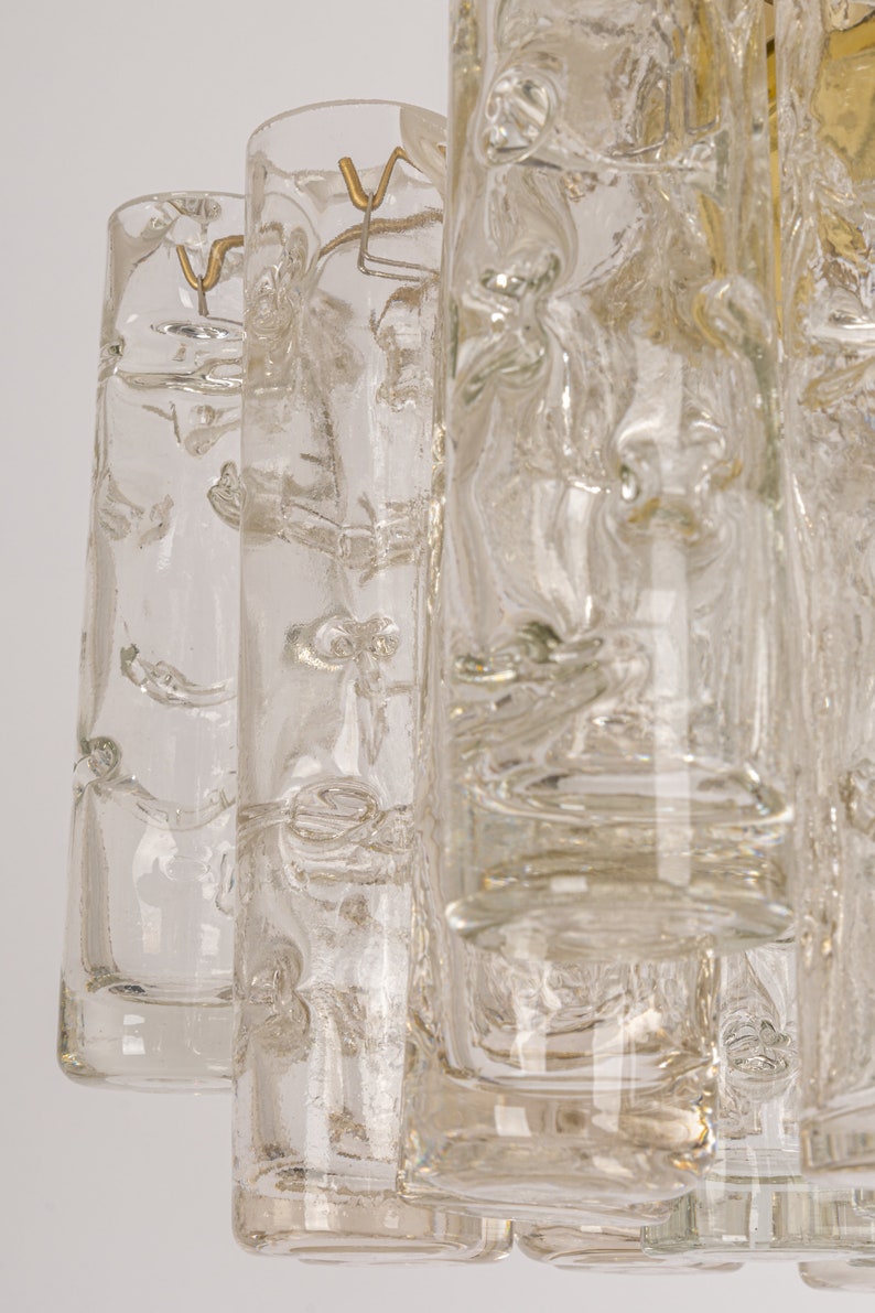 May include: A close-up of a clear glass chandelier with a textured surface. The chandelier has multiple tiers of glass cylinders.