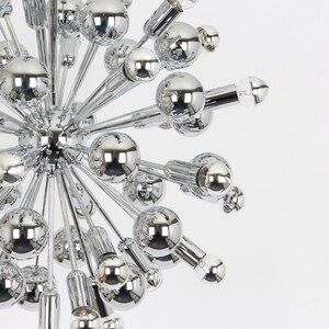 Op de afbeelding: Een chromen Sputnik-kroonluchter met meerdere ronde lampen die naar buiten uitstrekken vanaf een centraal punt.