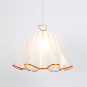 May include: A white glass pendant light with a ruffled edge and a gold metal hook. The light has a warm, amber-colored trim around the edge.
