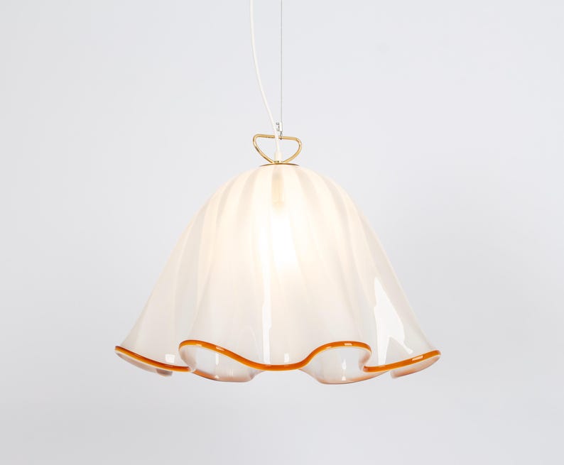 May include: A white glass pendant light with a ruffled edge and a gold metal hook. The light has a warm, amber-colored trim around the edge.