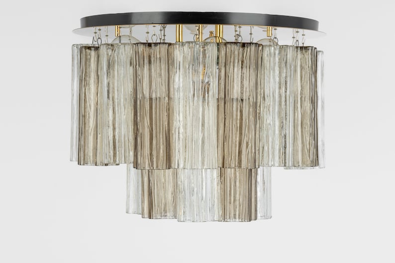 May include: A ceiling light fixture with a black circular base and multiple rows of clear and frosted glass tubes.