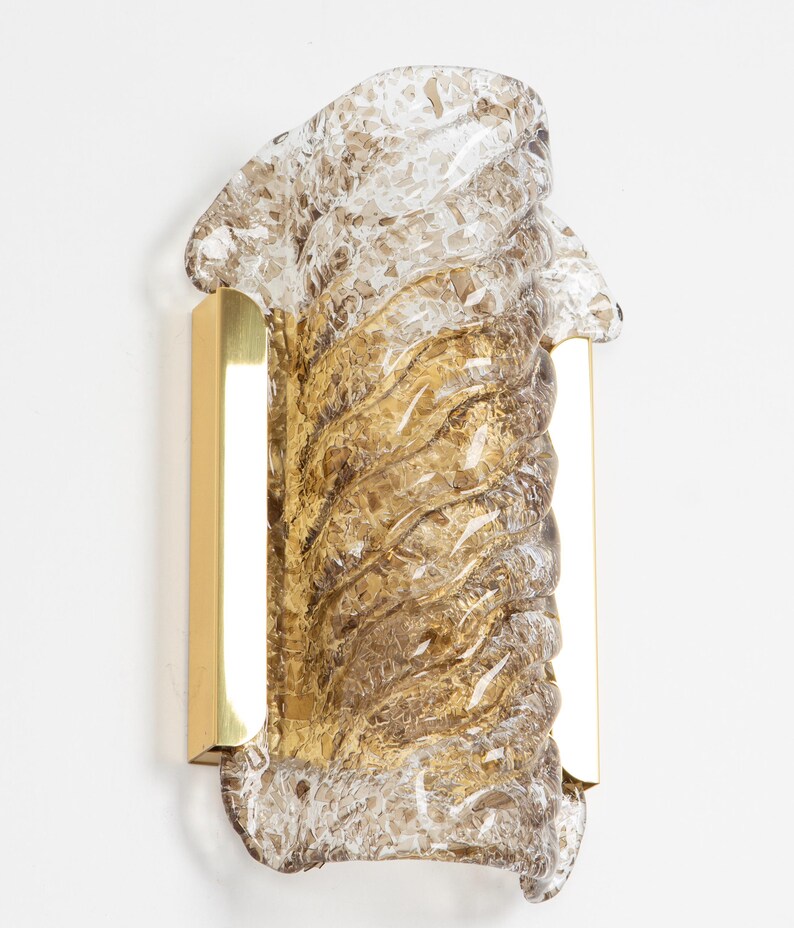 May include: A brown glass wall sconce with a textured, wavy design. The sconce is mounted on a brass bracket.