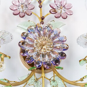 Puede incluir: Una l&aacute;mpara de pared dorada con dos bombillas de estilo vela y flores de cristal. Las flores son en tonos de rosa, morado y verde.