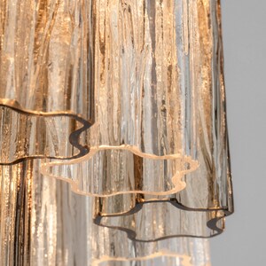 May include: A close-up of a multi-tiered glass chandelier with a rippled, textured surface. The glass is clear with a slight amber hue. The chandelier has a modern design and would be a stylish addition to any home.