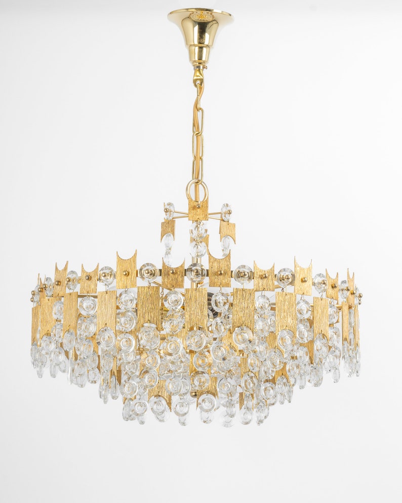 Peut inclure: Un lustre de couleur or avec un design g&eacute;om&eacute;trique et des accents de cristal transparent. Le lustre a une forme circulaire et est suspendu &agrave; une cha&icirc;ne.