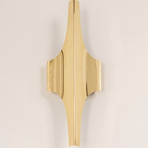 May include: A gold-coloured metal wall sconce with a geometric design. The sconce has a pointed top and a curved bottom.