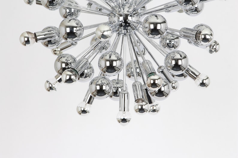 Op de afbeelding: Een chromen kroonluchter met meerdere ronde lampen die naar buiten uitstrekken vanaf een centraal punt. De lampen zijn allemaal even groot en zijn in een symmetrisch patroon gerangschikt.