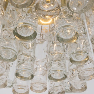 May include: A close-up of a clear glass chandelier with multiple cylindrical and round glass pieces. The chandelier has a gold metal frame.