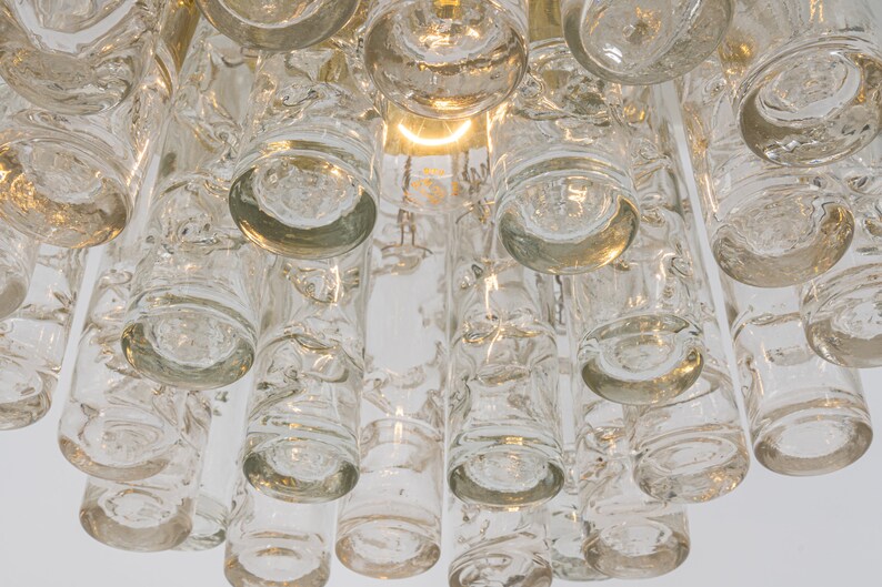 May include: A close-up of a clear glass chandelier with multiple cylindrical and round glass pieces. The chandelier has a gold metal frame.