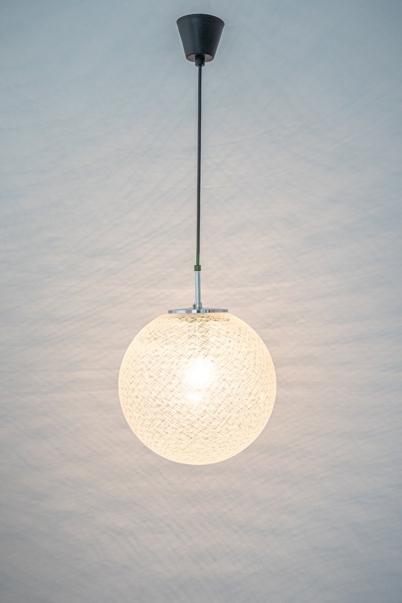 Peut inclure: Un luminaire rond blanc suspendu avec un abat-jour tiss&eacute;. La lumi&egrave;re est allum&eacute;e et diffuse une lueur chaude.
