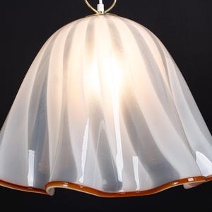 May include: White glass pendant light fixture with a ruffled, wavy design and a brown trim around the bottom edge.
