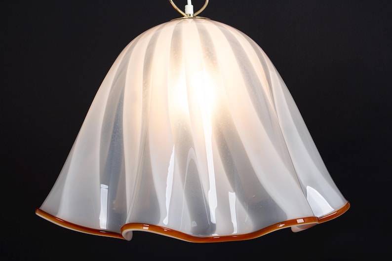 May include: White glass pendant light fixture with a ruffled, wavy design and a brown trim around the bottom edge.