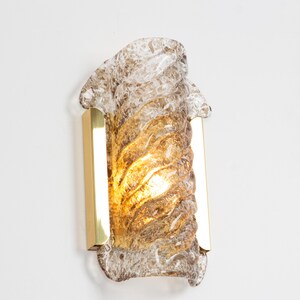 May include: A brass wall sconce with a clear and amber glass shade. The glass shade has a swirling, textured design.