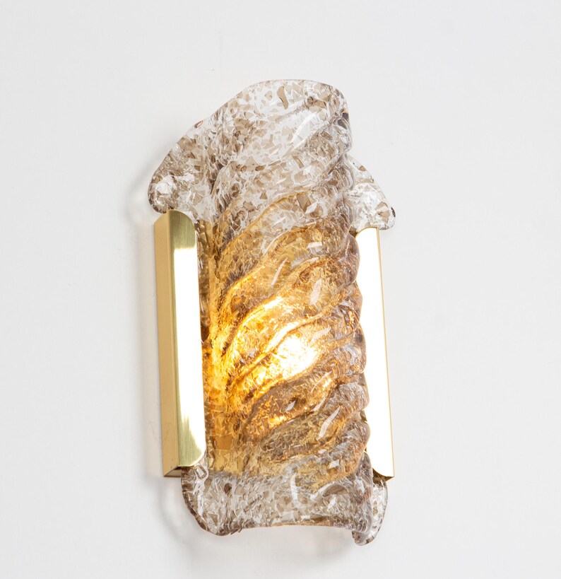 May include: A brass wall sconce with a clear and amber glass shade. The glass shade has a swirling, textured design.
