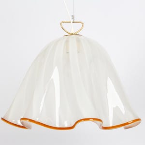 May include: A white glass pendant light with a gold metal canopy and a ruffled, scalloped edge. The light has a warm, amber-colored trim.
