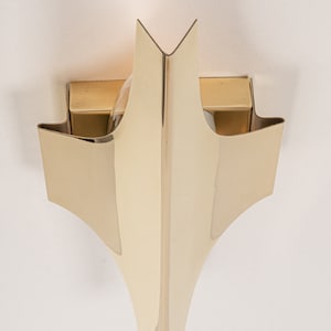 May include: A gold-toned wall sconce with a geometric design. The sconce has two light bulbs and a pointed, triangular shape.