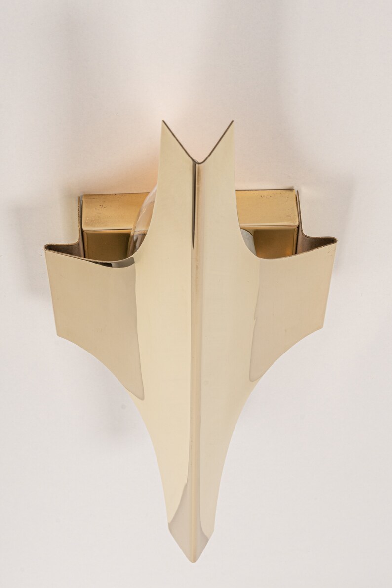 May include: A gold-toned wall sconce with a geometric design. The sconce has two light bulbs and a pointed, triangular shape.
