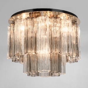 May include: A round, multi-tiered chandelier with clear glass rods. The chandelier has a polished brass finish and is illuminated by multiple light bulbs.