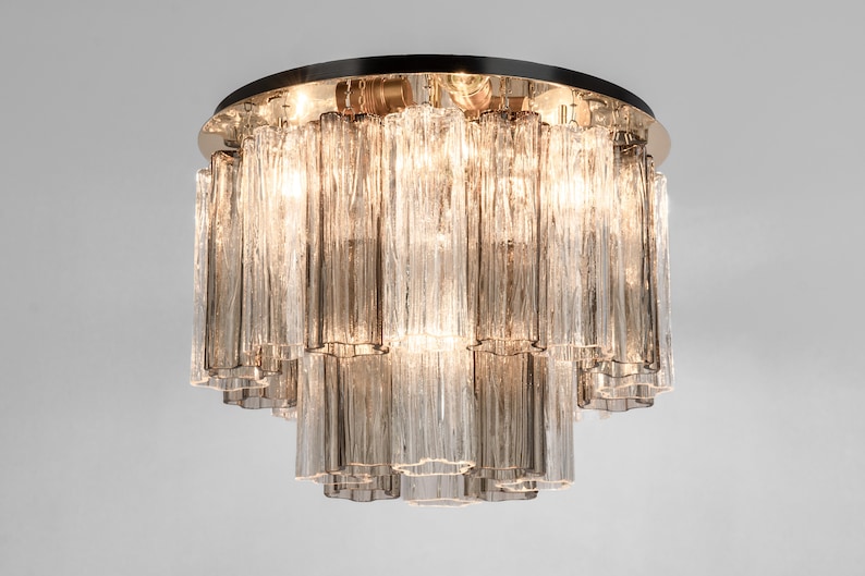 May include: A round, multi-tiered chandelier with clear glass rods. The chandelier has a polished brass finish and is illuminated by multiple light bulbs.