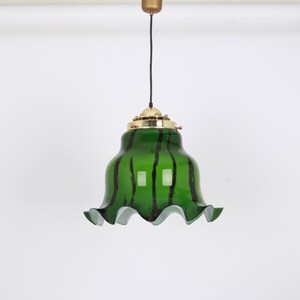 May include: A green glass pendant light with black stripes and a ruffled edge. The light fixture has a brass finish.
