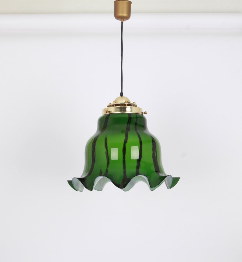 May include: A green glass pendant light with black stripes and a ruffled edge. The light fixture has a brass finish.