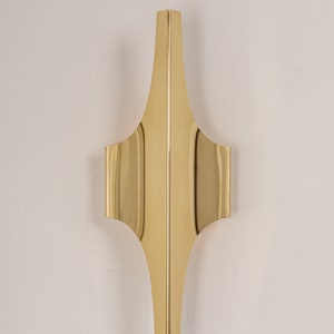 May include: A gold metal wall sconce with a geometric design. The sconce has a pointed top and a wide base.
