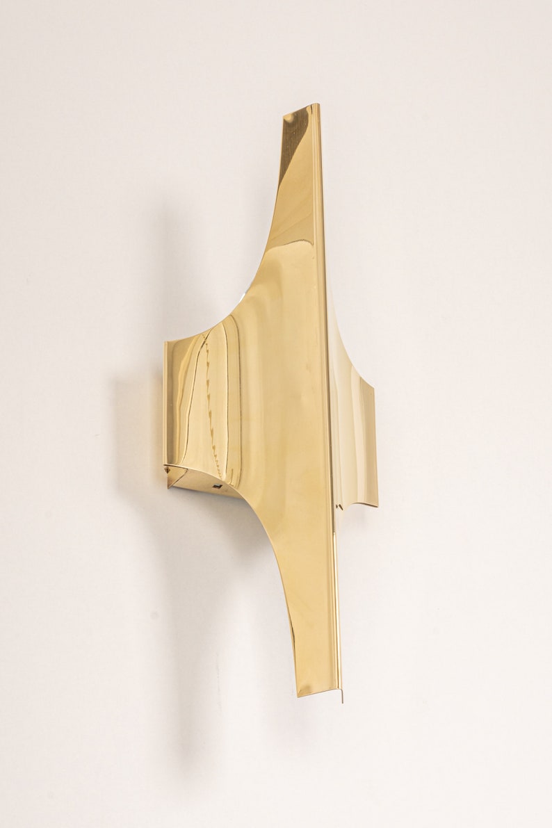May include: A gold-toned wall sconce with a geometric design. The sconce has a curved shape and a sharp point at the top.