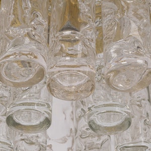 May include: Close-up of a clear glass chandelier with multiple cylindrical glass pieces hanging from a brass frame.