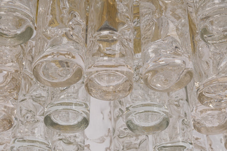 May include: Close-up of a clear glass chandelier with multiple cylindrical glass pieces hanging from a brass frame.