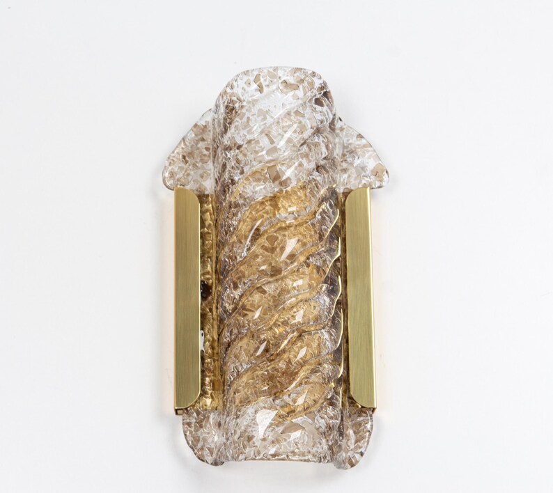 May include: A brass wall sconce with a clear glass shade featuring a textured, swirling pattern. The glass shade is a light brown color.