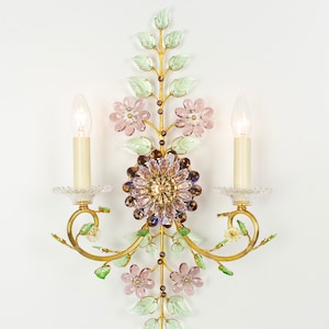 Puede incluir: Una l&aacute;mpara de pared dorada con un dise&ntilde;o floral. La l&aacute;mpara tiene dos bombillas de estilo vela y presenta flores y hojas de vidrio rosa y verde.
