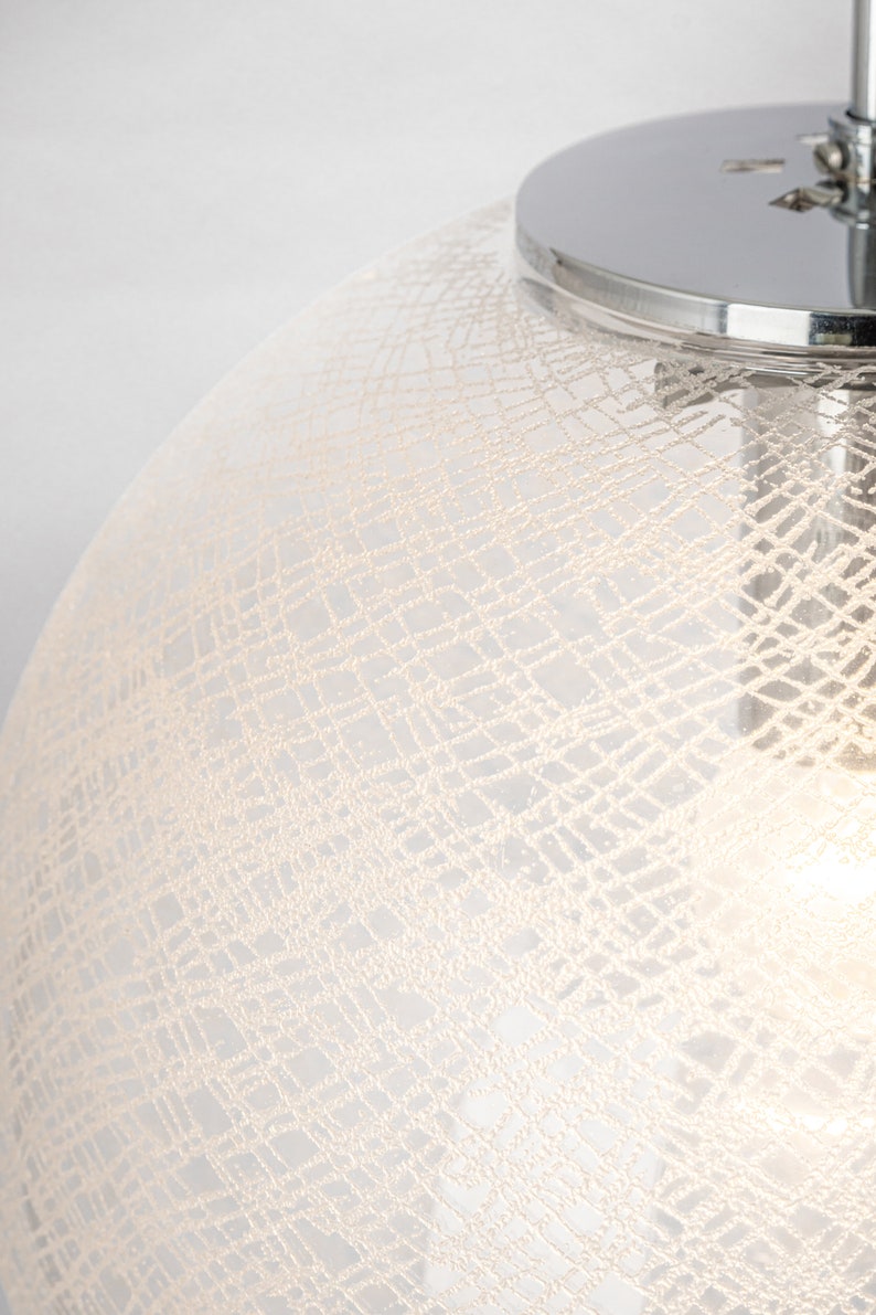 Peut inclure: Un luminaire suspendu en verre blanc avec un dessus chrom&eacute; et un motif d&eacute;licat tiss&eacute;.