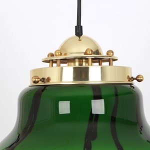May include: A green glass pendant light with black stripes and a brass top with a dome-shaped shade. The light has a black cord.
