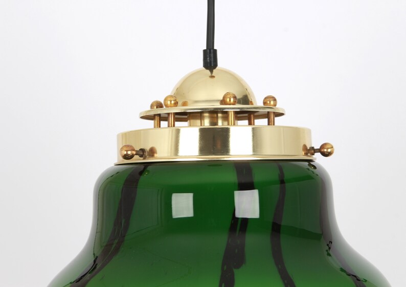 May include: A green glass pendant light with black stripes and a brass top with a dome-shaped shade. The light has a black cord.