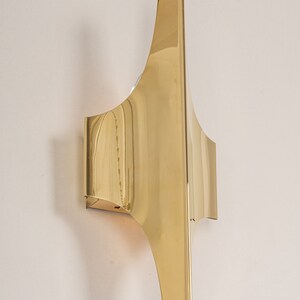 May include: A gold-toned metal wall sconce with a unique, geometric design. The sconce has a curved, angular shape and a polished finish.