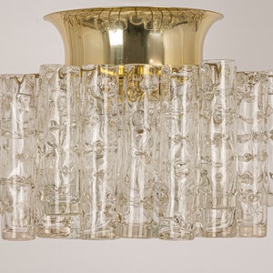 May include: A brass and glass ceiling light fixture with a circular base and multiple clear glass cylinders. The glass cylinders have a textured surface.
