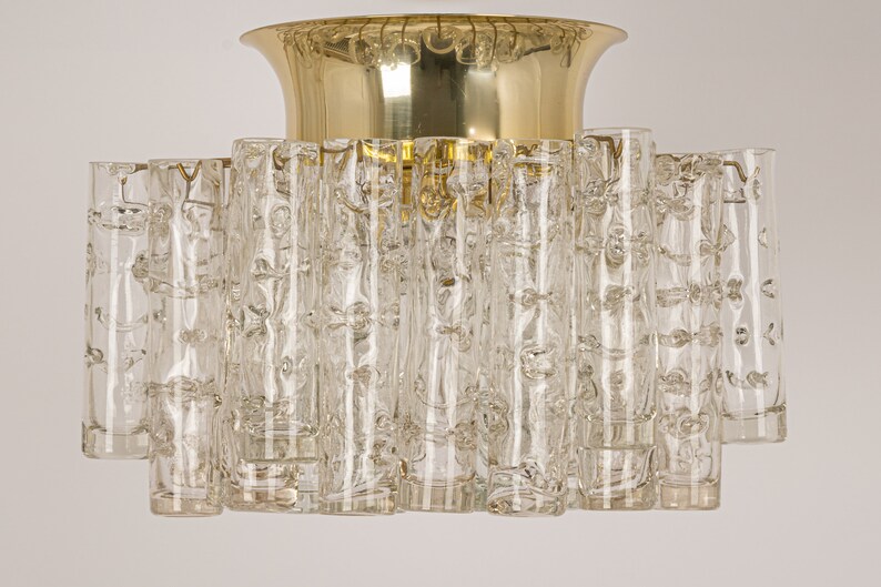 May include: A brass and glass ceiling light fixture with a circular base and multiple clear glass cylinders. The glass cylinders have a textured surface.