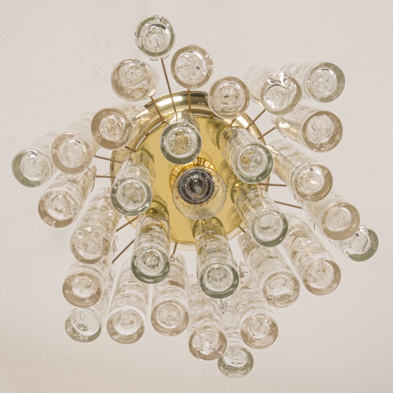 May include: A gold-toned chandelier with clear glass cylinders and round glass bulbs. The chandelier has a circular base and is suspended from the ceiling.