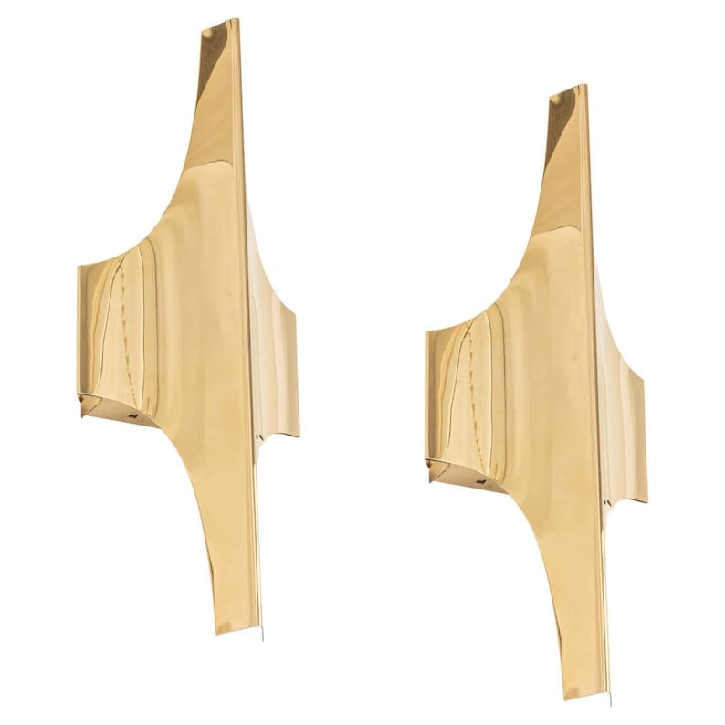 May include: A pair of gold-toned wall sconces with a unique, abstract design. The sconces have a geometric shape with curved edges and a smooth, polished finish.