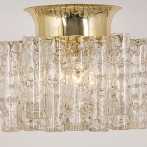 May include: A brass and glass ceiling light fixture with a circular base and a central dome. The fixture is made up of many clear glass tubes with a textured surface.