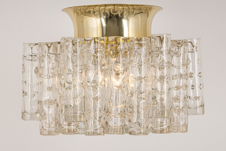 May include: A brass and glass ceiling light fixture with a circular base and a central dome. The fixture is made up of many clear glass tubes with a textured surface.