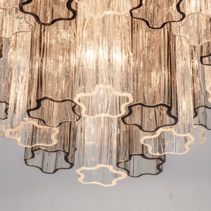 May include: A multi-tiered chandelier with clear glass tubes and a scalloped design. The chandelier has a warm, golden hue.