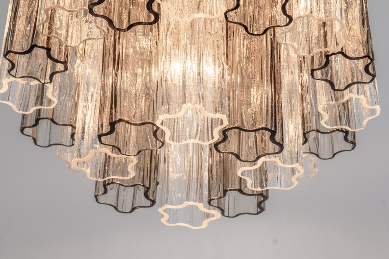 May include: A multi-tiered chandelier with clear glass tubes and a scalloped design. The chandelier has a warm, golden hue.