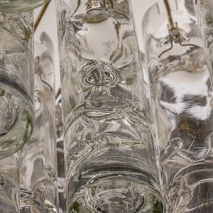 May include: A close-up of a chandelier made of clear glass cylinders. The cylinders are suspended from a metal frame and have a textured, rippled surface.