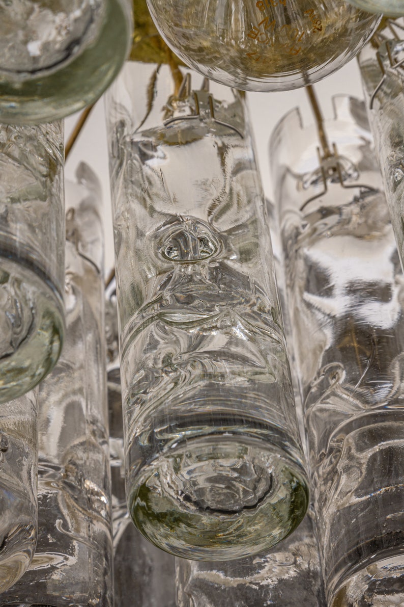 May include: A close-up of a chandelier made of clear glass cylinders. The cylinders are suspended from a metal frame and have a textured, rippled surface.