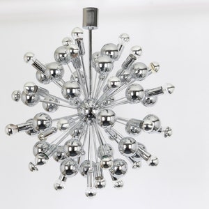Op de afbeelding: Een chromen Sputnik-kroonluchter met meerdere ronde lampen die naar buiten uitstrekken vanaf een centraal punt.