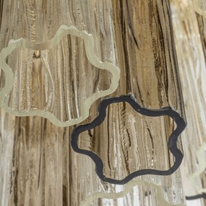 May include: Close-up of a glass chandelier with multiple tiers of clear glass tubes. The tubes have a textured, rippled surface and are joined together with black metal rings.