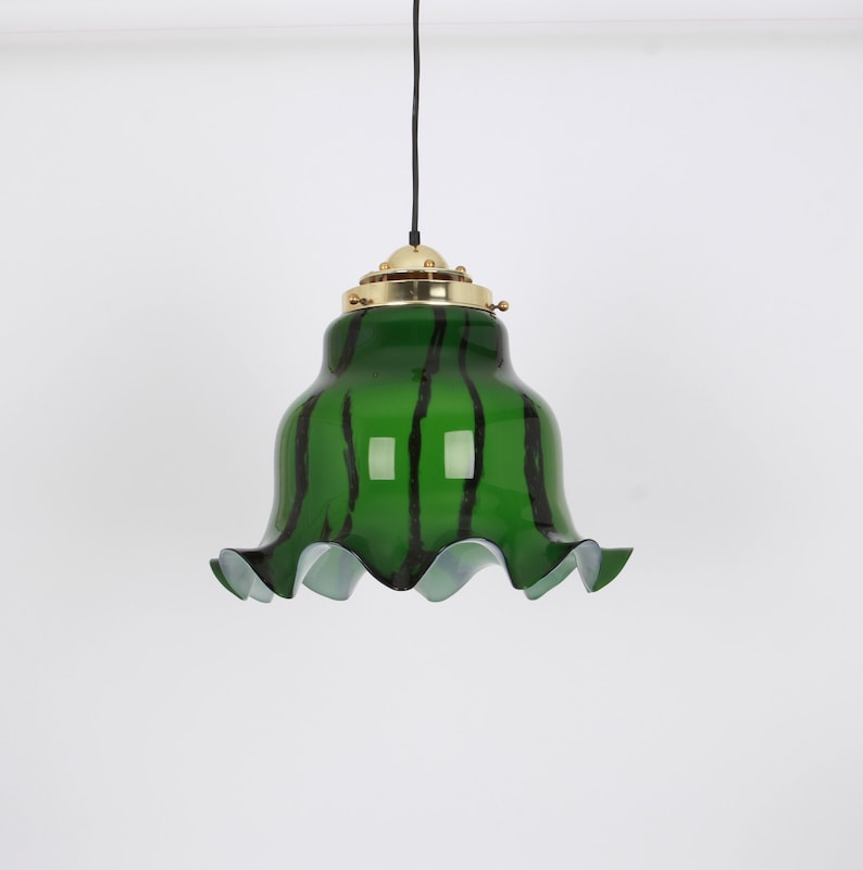 May include: A green glass pendant light with black stripes and a ruffled edge. The light fixture has a brass top and a black cord.