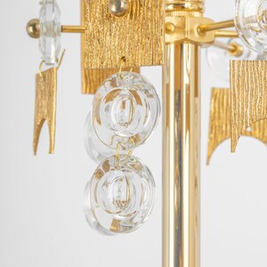 Peut inclure: Un lustre dor&eacute; avec des cristaux de verre transparents suspendus aux bras. Le lustre a un design textur&eacute; et g&eacute;om&eacute;trique.