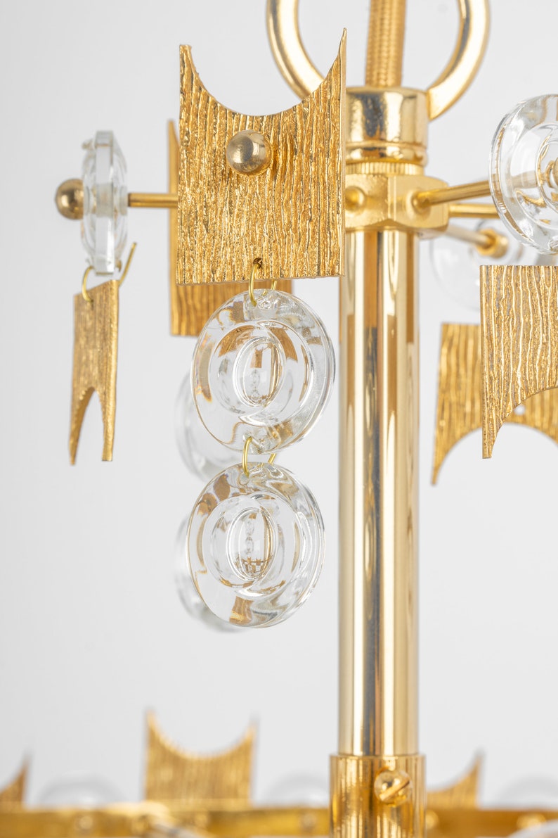 Peut inclure: Un lustre dor&eacute; avec des cristaux de verre transparents suspendus aux bras. Le lustre a un design textur&eacute; et g&eacute;om&eacute;trique.